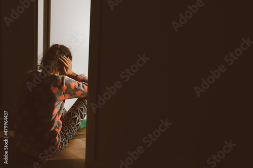 A little girl huddled in a corner and cries, covering her eyes and ears with her hands, because her parents are quarreling. Family problem, violation of children\'s rights