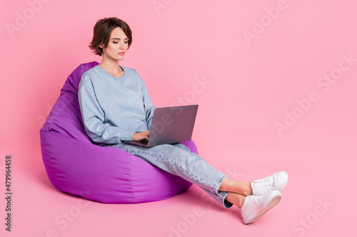 Full body photo of strict young lady sit type latop wear pullover jeans sneakers isolated on pink background