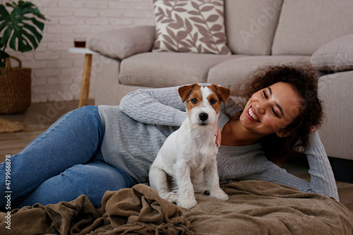 Portrait of young beautiful black woman with her adorable wire haired Jack Russel terrier puppy at home. Loving girl with rough coated pup having fun on the couch. Background, close up, copy space.