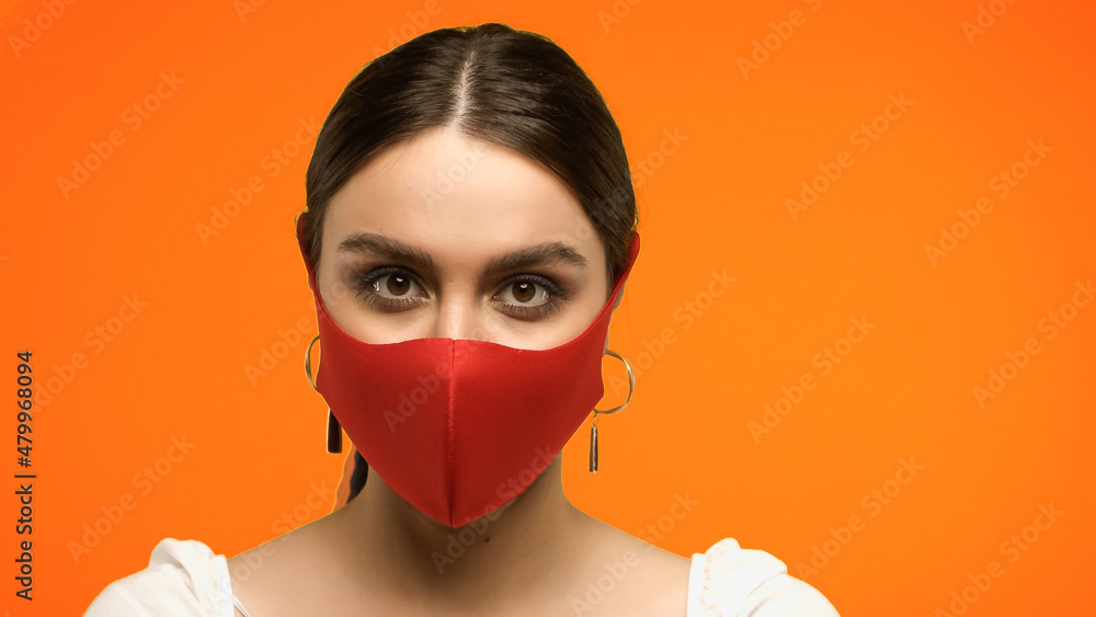 Young brunette woman in blouse and protective mask looking at camera isolated on orange. Young brunette woman in blouse and protective mask looking at camera isolated on orange.