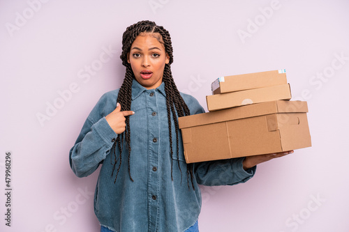 black afro woman looking shocked and surprised with mouth wide open, pointing to self. packages box concept photo