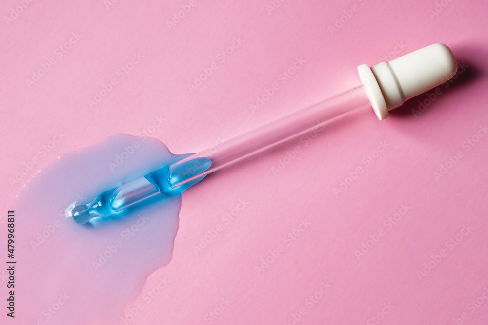 Blue drops of transparent liquid near pipette on pink background Blue drops of transparent liquid near pipette on pink background