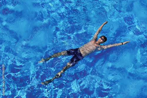 Young caucasian man floating on blue water in swimming pool. Top view. Summer vacation, relaxation, tourist on vacation © Анастасия Бурлакова