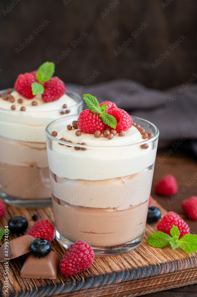 Dessert three chocolate in a glass jar with fresh blueberries, raspberries and blackberries on top on a dark wooden background. Dessert with three layers of different taste. Copy space. Dessert three chocolate in a glass jar with fresh blueberries, raspberries and blackberries on top on a dark wooden background. Dessert with three layers of different taste. Copy space.
