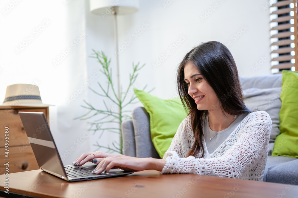 Beautiful young woman working on laptop computer while sitting at the living room Beautiful young woman working on laptop computer while sitting at the living room