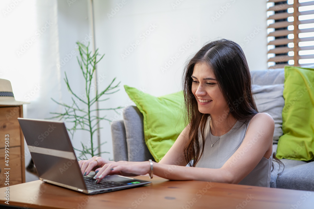 Beautiful young woman working on laptop computer while sitting at the living room Beautiful young woman working on laptop computer while sitting at the living room