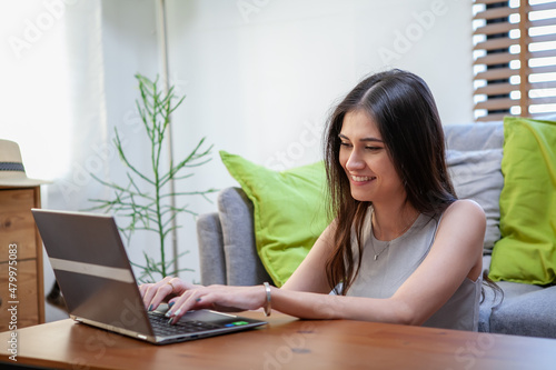 Beautiful young woman working on laptop computer while sitting at the living room