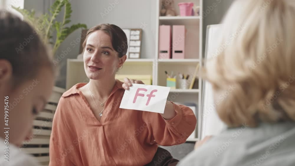 Medium slowmo shot of young female speech therapist teaching alphabet to group of children in classroom Medium slowmo shot of young female speech therapist teaching alphabet to group of children in classroom