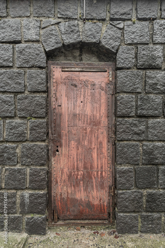 Ancient stone arch with a rusty metal door. © Dmytro
