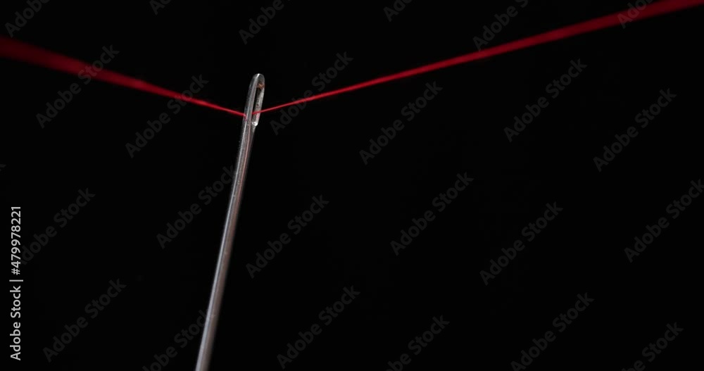 Swift fingers pull the red thread through the eye of the needle Swift fingers pull the red thread through the eye of the needle