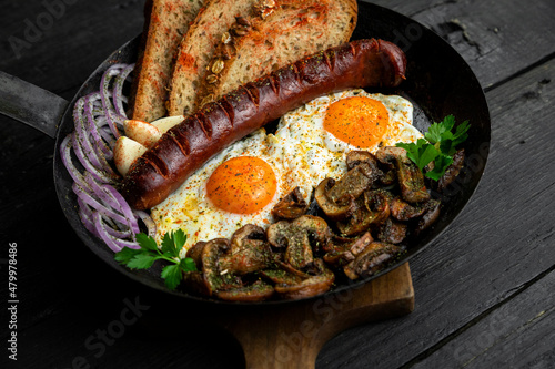 Fried eggs and sausage with mushrooms served in cast iron pan in the kitchen