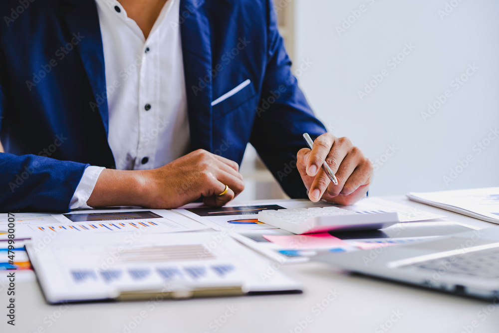 Asian male finance staff is calculating by using a calculator. Investment results to report to his boss at the meeting. On the table in the office, the concept of calculating investment results Asian male finance staff is calculating by using a calculator. Investment results to report to his boss at the meeting. On the table in the office, the concept of calculating investment results