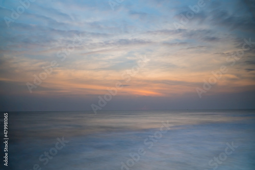 Beautiful long exposure of an amazing sunset from smooth wavy sea and cloud. orange horizon with sunrise sky. © pornpun