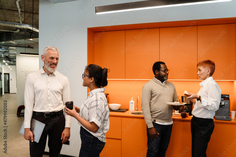 Multiracial colleagues talking and having sandwiches in office Multiracial colleagues talking and having sandwiches in office