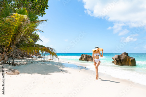 Fototapeta Naklejka Na Ścianę i Meble -  Slender woman wearing beach hat at tropical beach, Seychelles – vacation. Summer vacations on picture perfect tropical beach concept.