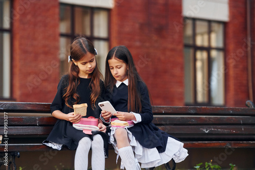 Two schoolgirls is sitting outside together near school building