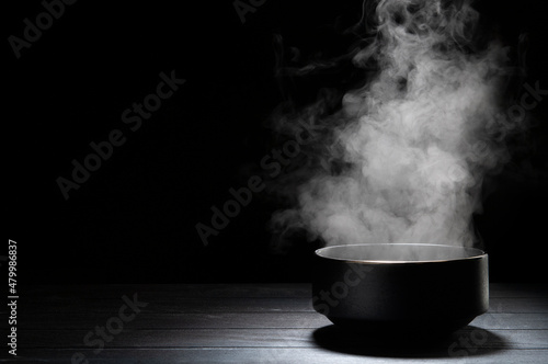 Bowl of hot soup with steaming on wooden table on black background.
