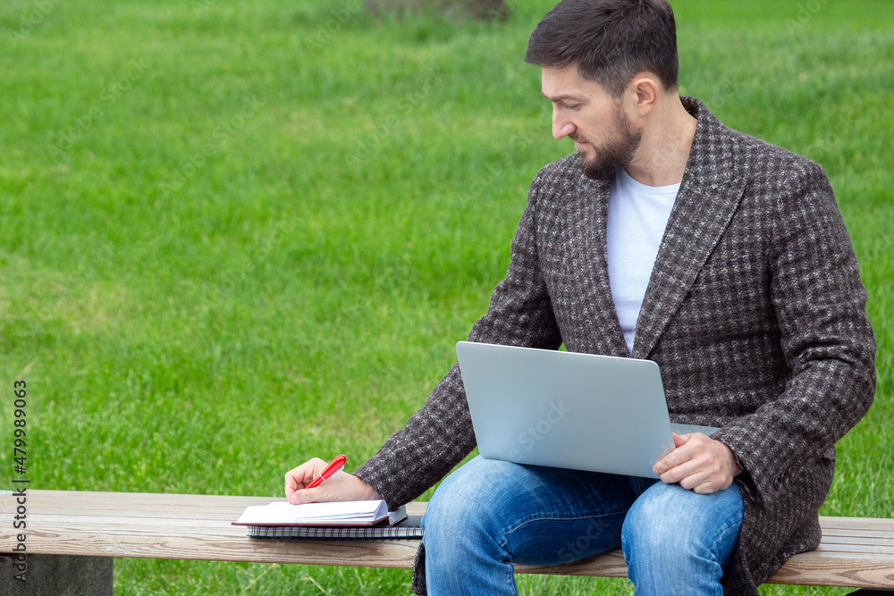 Successful businessman sits on a city bench and is engaged in business with documents and laptop Successful businessman sits on a city bench and is engaged in business with documents and laptop