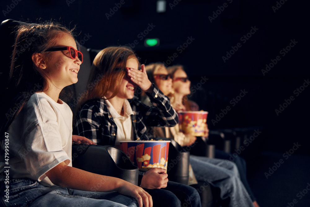 With popcorn. Group of kids sitting in cinema and watching movie together With popcorn. Group of kids sitting in cinema and watching movie together