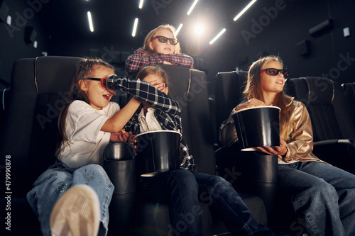 Eating popcorn. Group of kids sitting in cinema and watching movie together