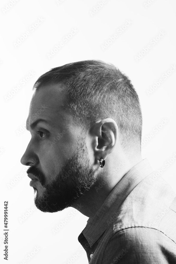 Fototapeta premium Emotive profile portrait of bearded charismatic muscular 40 years old man sitting over white background. Short haircut. Black and white studio shot. Text space