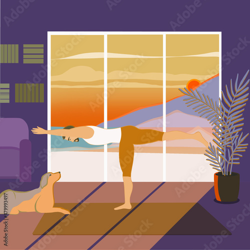 A sporty handsome man standing in Warrior 3 or Virabhadrasana III pose in the sunny room with a beautiful view with a dog sitting next to him. Working out indoors, man is in balancing stick pose.