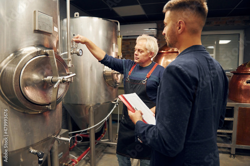 Senior man and young worker with document is standing in the storage beer room