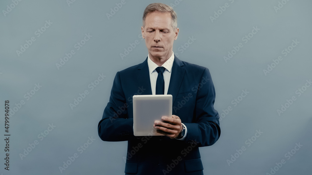 Mature manager in formal wear using digital tablet isolated on grey.