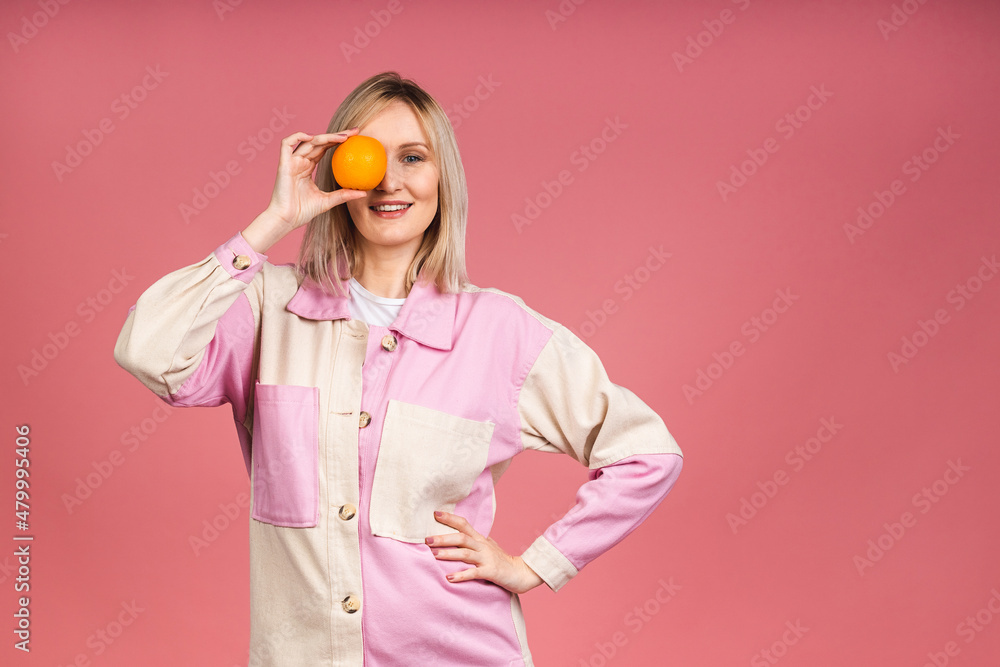 Smiling young excited blonde woman looking at camera while holding an orange fruit isolated over pink background. Diet healthy eating. Smiling young excited blonde woman looking at camera while holding an orange fruit isolated over pink background. Diet healthy eating.