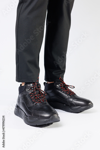 Stylish leather black short men's autumn sneakers on a white background on men's legs. Sneakers winter collection 2022.