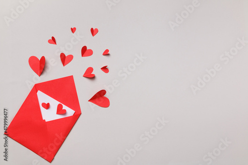 Red paper envelope with a white note inside and hearts on a gray pastel background. Love letter for Valentine's Day. Flat lay, top view. © Olga