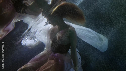 romantic and mysterious underwater shot with elegant young woman floating and playing with dress