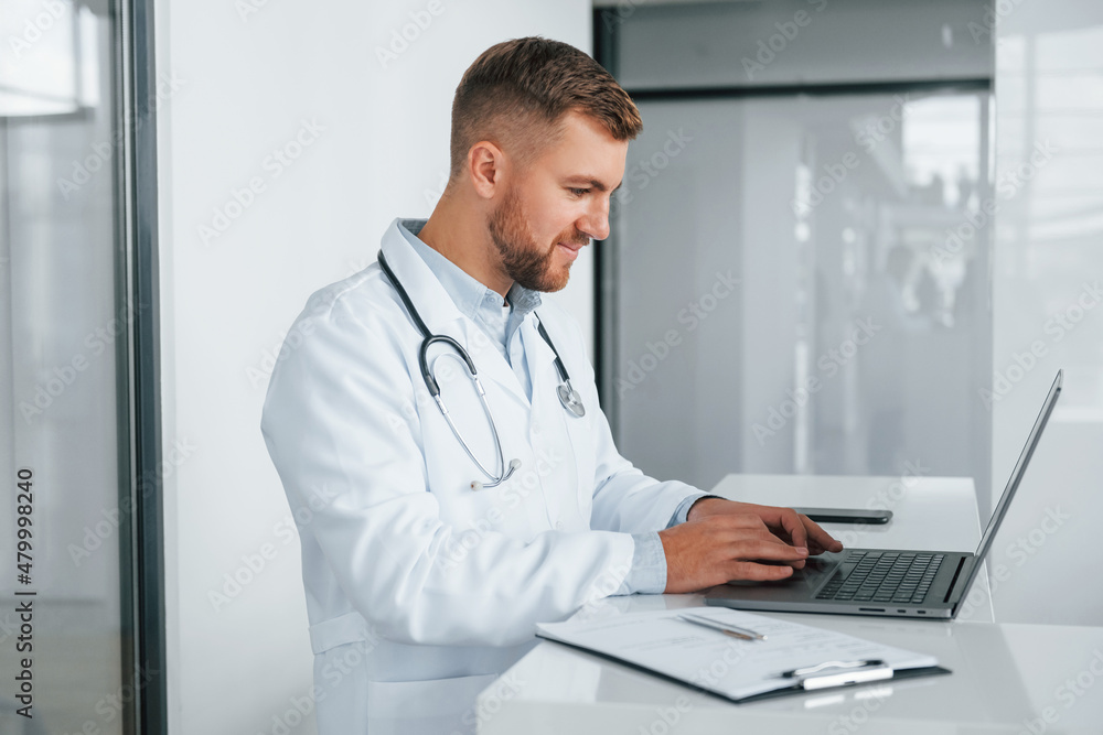 Using laptop. Professional medic in white coat is in the clinic Using laptop. Professional medic in white coat is in the clinic