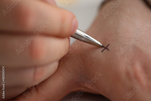Man makes x note with cross with pen on hand  closeup