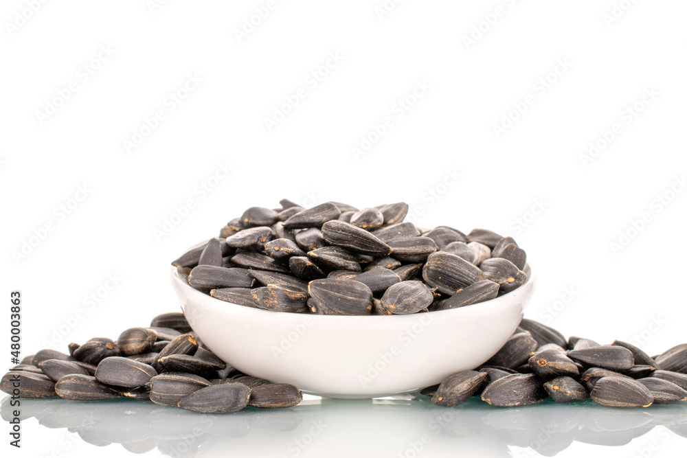 Many fragrant sunflower seeds with a white ceramic saucer, close-up, isolated on white. Many fragrant sunflower seeds with a white ceramic saucer, close-up, isolated on white.