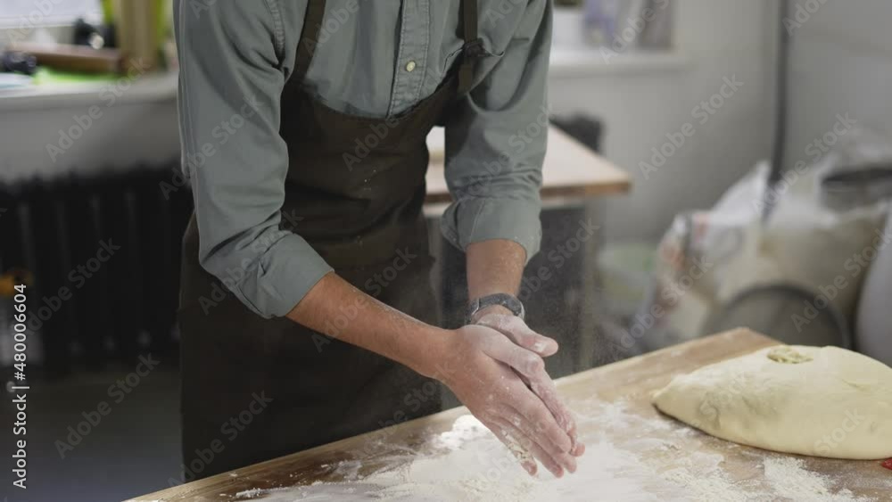 Unrecognizable male baker claps and scatters white flour in the air. Young man making homemade bread claps with a handful of organic whole wheat flour in each hand. Slow motion, close up Unrecognizable male baker claps and scatters white flour in the air. Young man making homemade bread claps with a handful of organic whole wheat flour in each hand. Slow motion, close up
