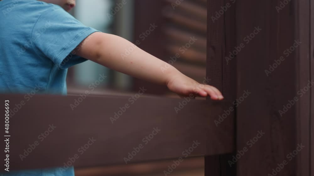 Toddler boy in blue t-shirt touches wet wooden beam of handrail walking along veranda deck at cottage house extreme closeup slow motion Toddler boy in blue t-shirt touches wet wooden beam of handrail walking along veranda deck at cottage house extreme closeup slow motion