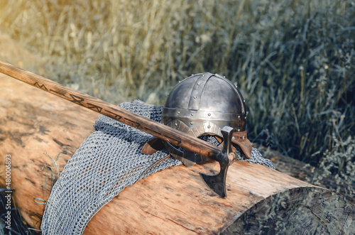 Metal chain mail, helmet and ax lie on a wooden log. Viking armor. Historical film concept.