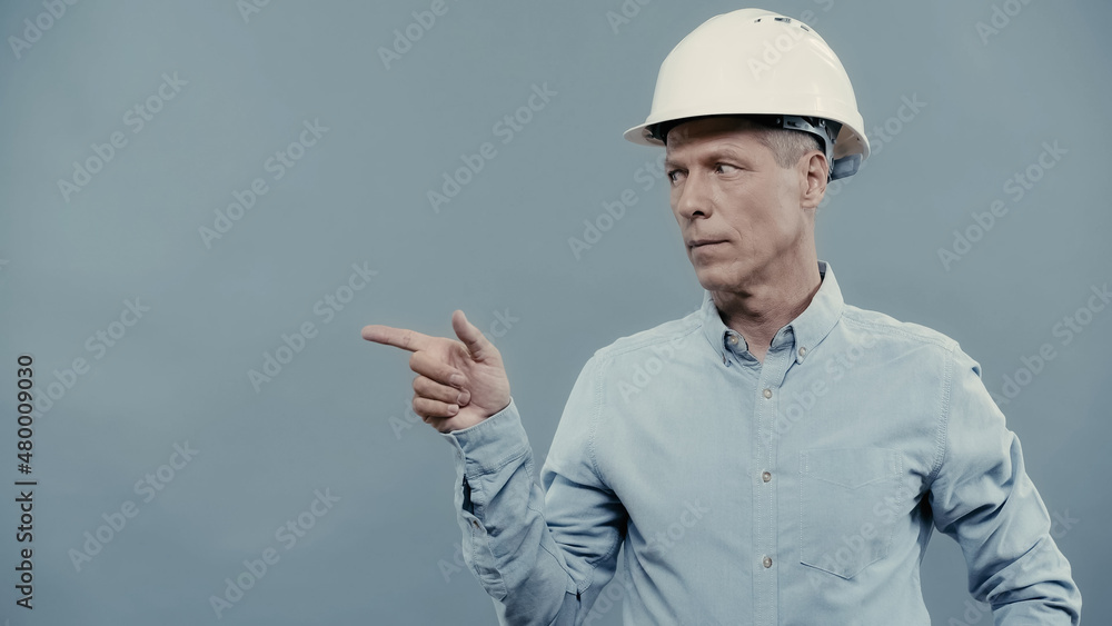 Middle aged businessman in hardhat pointing with finger isolated on grey. Middle aged businessman in hardhat pointing with finger isolated on grey.