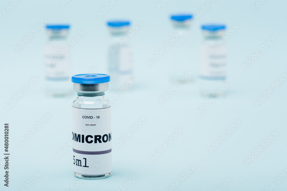 selective focus of covid-19 omicron variant vaccine near blurred vials on blue.