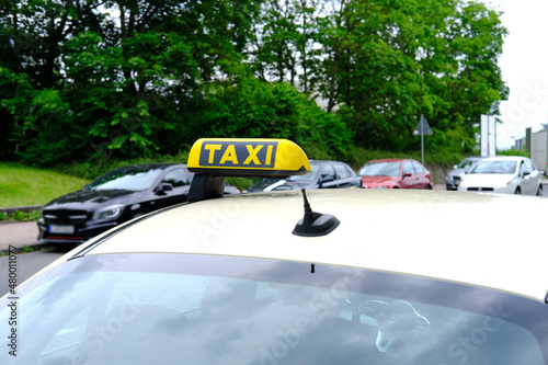 white passenger car with a yellow taxi sign on the roof at the top is waiting for its client, observes the rules of road, vehicles pass by, the concept of car services to population in city