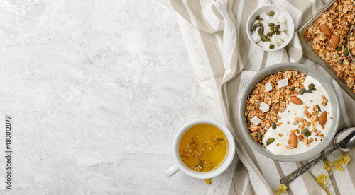 Fotografija Cooked granola muesli with yogurt, pumpkin seeds, almonds and coconut pieces in baking sheet and bouls with a spoon and herbal tea