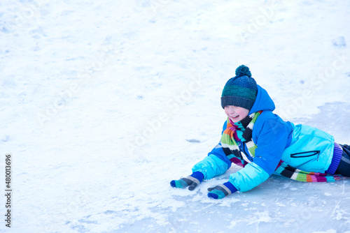  the boy rolled down the ice slide and lies on his stomach in the snow in winter 