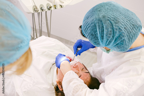 Photo from above of a professional dentist working with a patient teeth using instruments in uniform, mask and gloves.