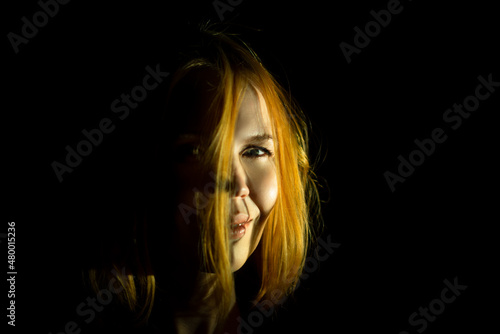 A middle-aged woman smiles mysteriously in the dark. Dark background. A woman of forty years old. Red hair.