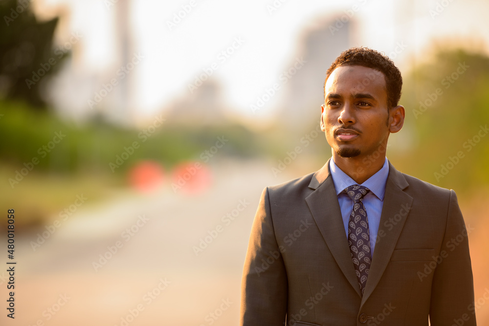 Handsome young black businessman wearing suit in city while thinking