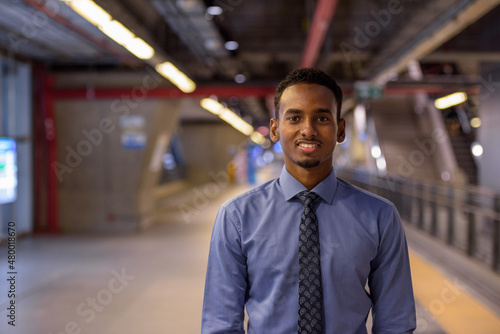 Canvas Print Handsome young black businessman smiling and wearing shirt and tie in station pl