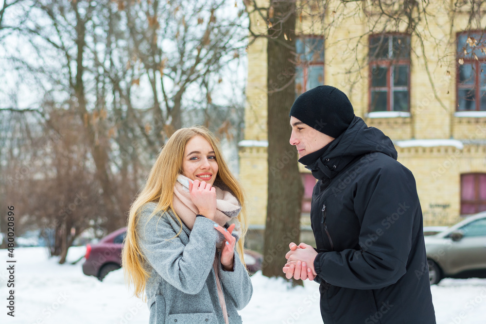 The man folded his arms pleadingly and looks at a beautiful girl in a winter park