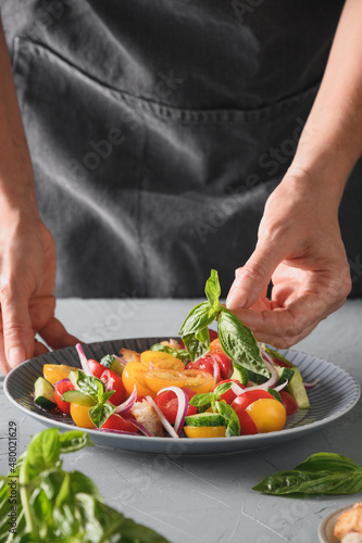 Woman cooking healthy italian Panzanella salad with fresh vegetables and crispy croutons.