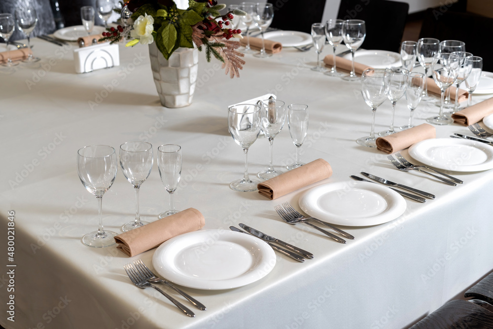 Close up new white porcelain tableware plates on white tablecloths and empty wine glasses ready for dinner.